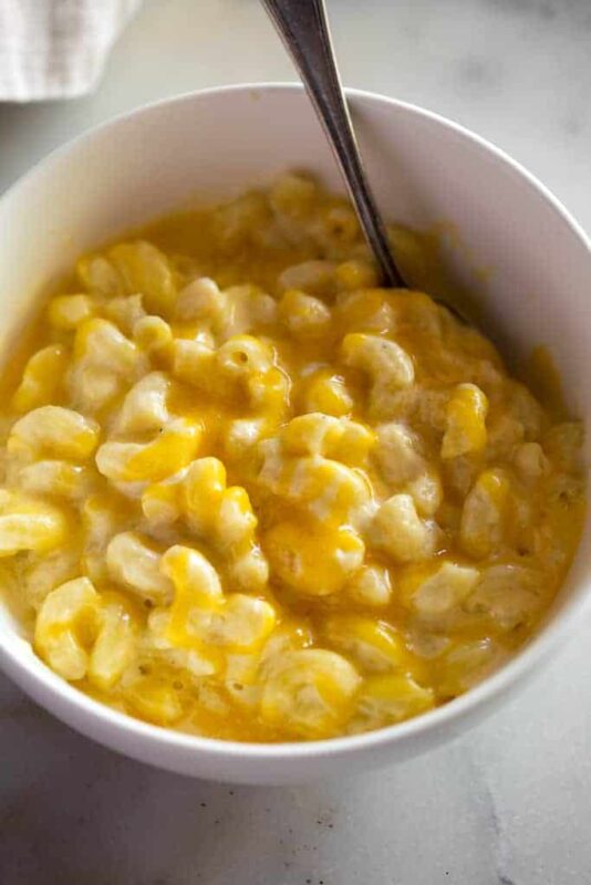 A white bowl with homemade mac and cheese in it and a spoon.