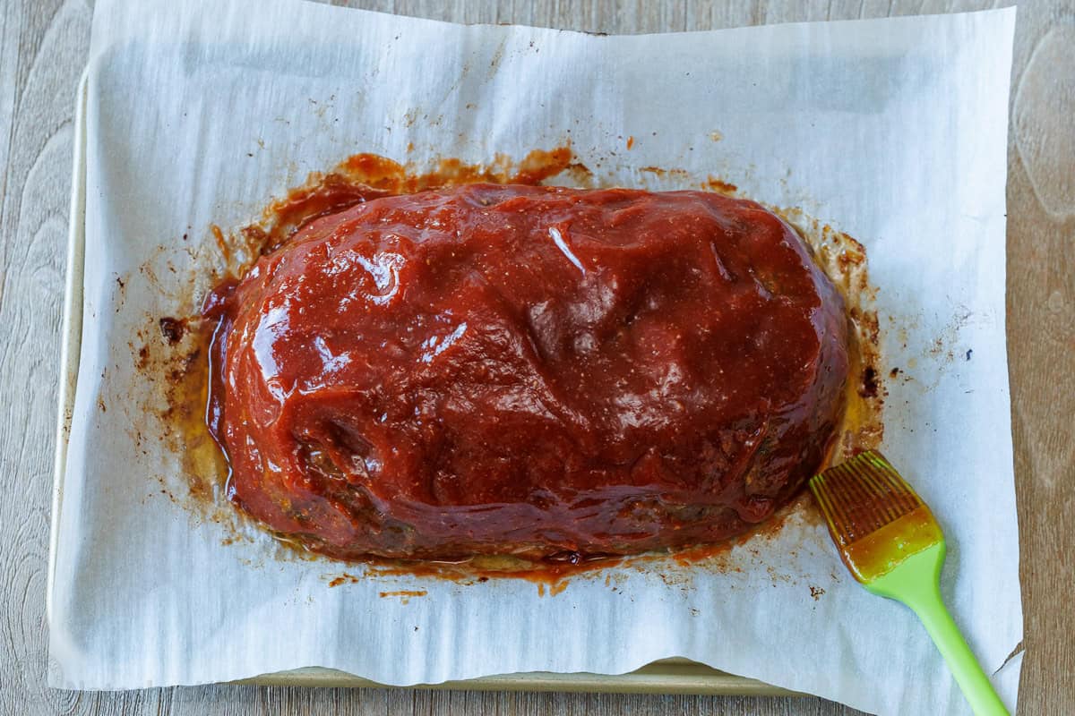 Brushing the sweet and tangy glaze over the partially baked meatloaf